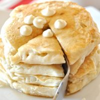 Using a fork to cut a bite from a stack of White Chocolate Chip Macadamia Nut Pancakes