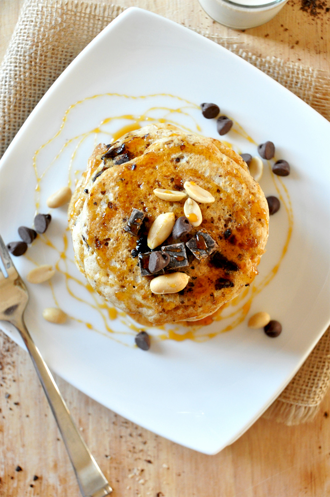 Tall stack of Vegan Snickers Pancakes topped with dark chocolate and peanuts