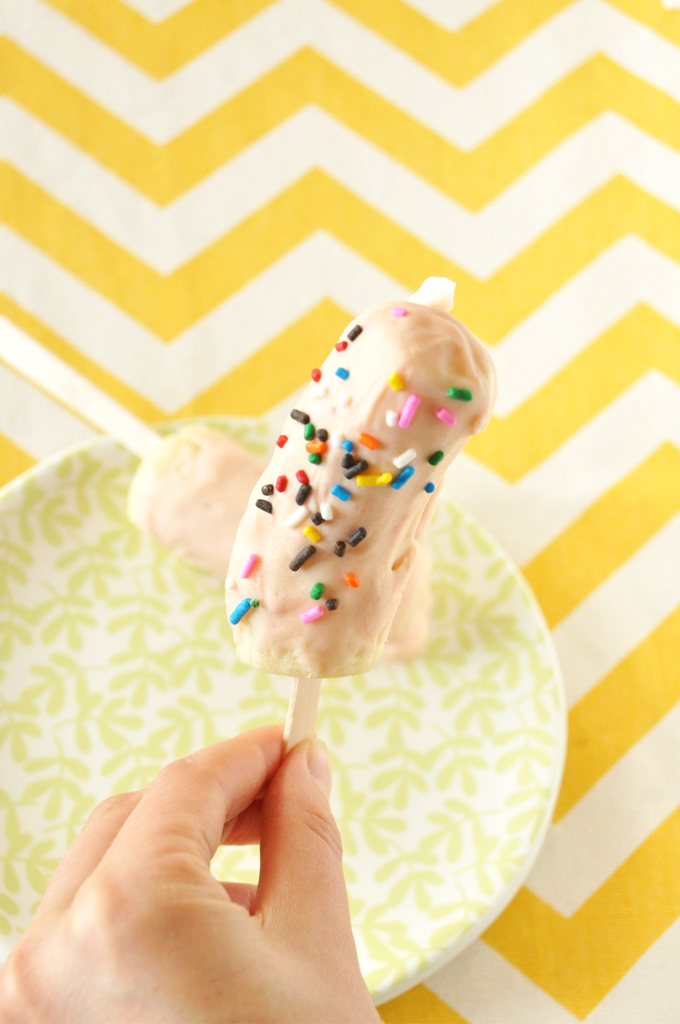 Strawberry Cake Magic Shell! by Minimalist Baker Holding up a banana pop topped with Strawberry Cake Magic Shell
