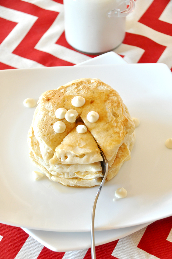 minimalist baker white chocolate chip pancakes!! Using a fork to cut into a stack of White Chocolate Macadamia Nut Pancakes