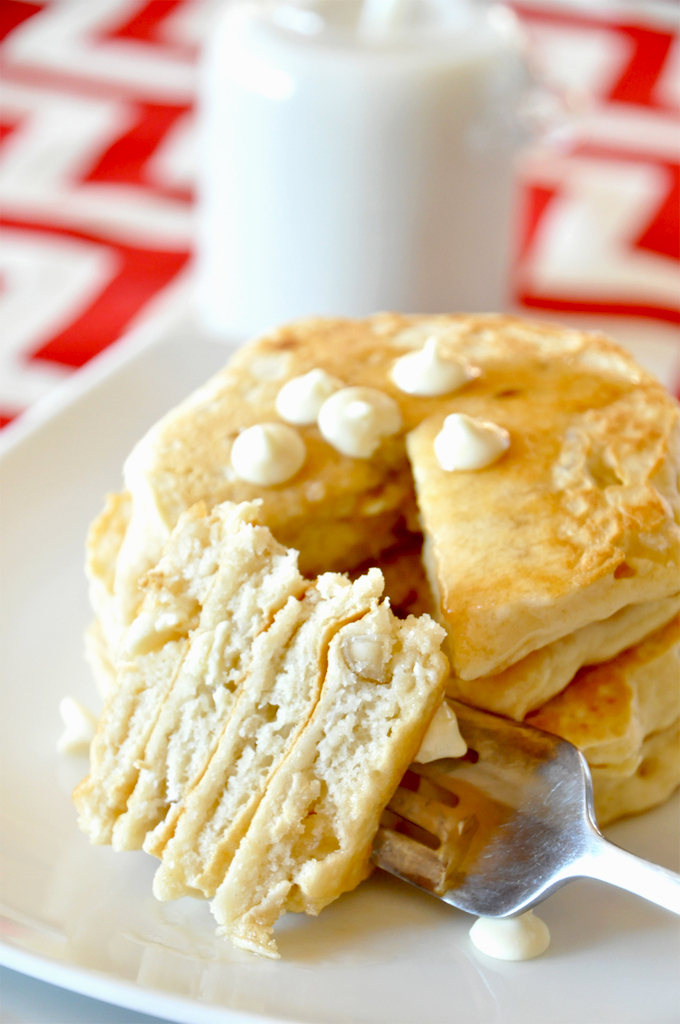 white chocolate macadamia nut pancakes! by Minimalist Baker. Big bite of White Chocolate Macadamia Nut Pancakes resting on a fork near the rest of the stack