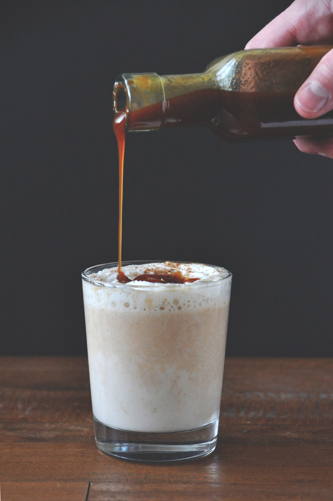 Drizzling homemade caramel sauce onto a glass of our Boozy Pumpkin White Hot Chocolate recipe