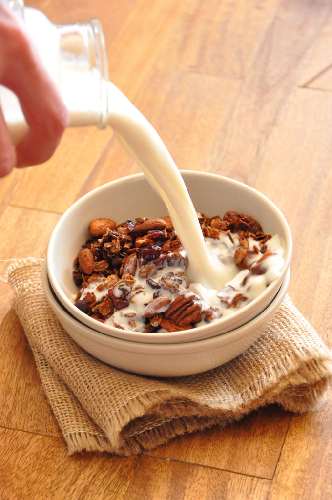 Coconut Honey Almond Granola Pouring milk into a stack of bowls with the top one filled with Coconut Granola