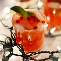 Glasses of homemade Pomegranate Lime Spritzers surrounded by Christmas lights