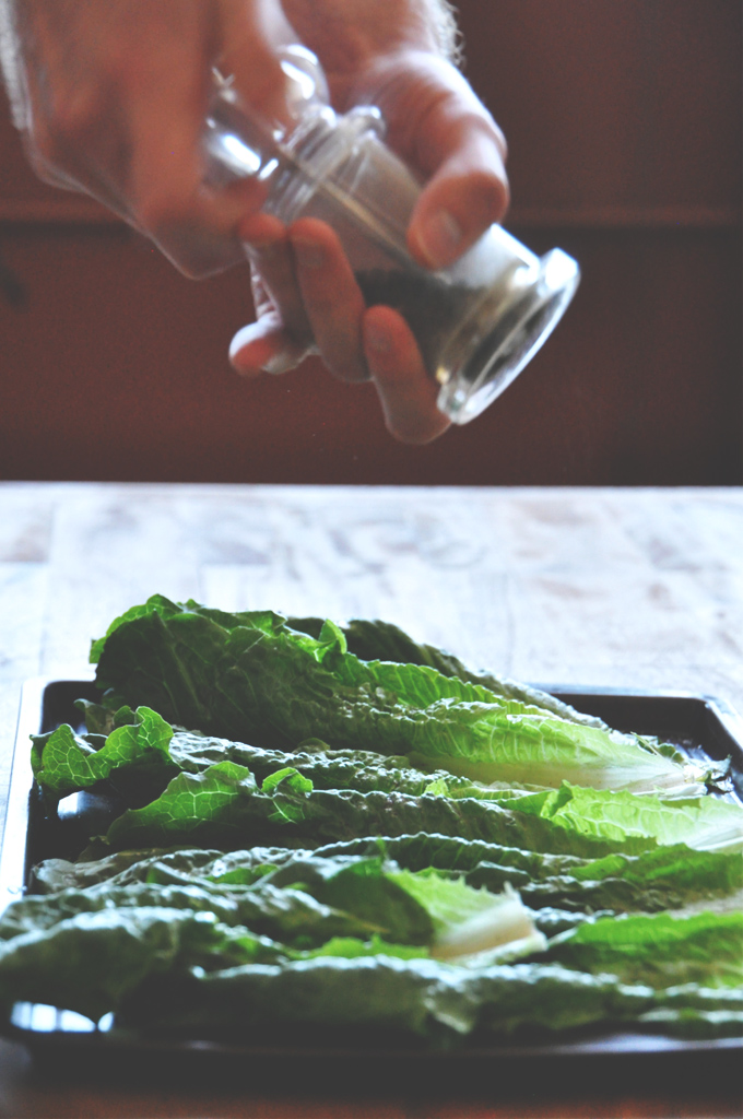 Using a pepper grinder to add black pepper onto a Grilled Romaine Salad