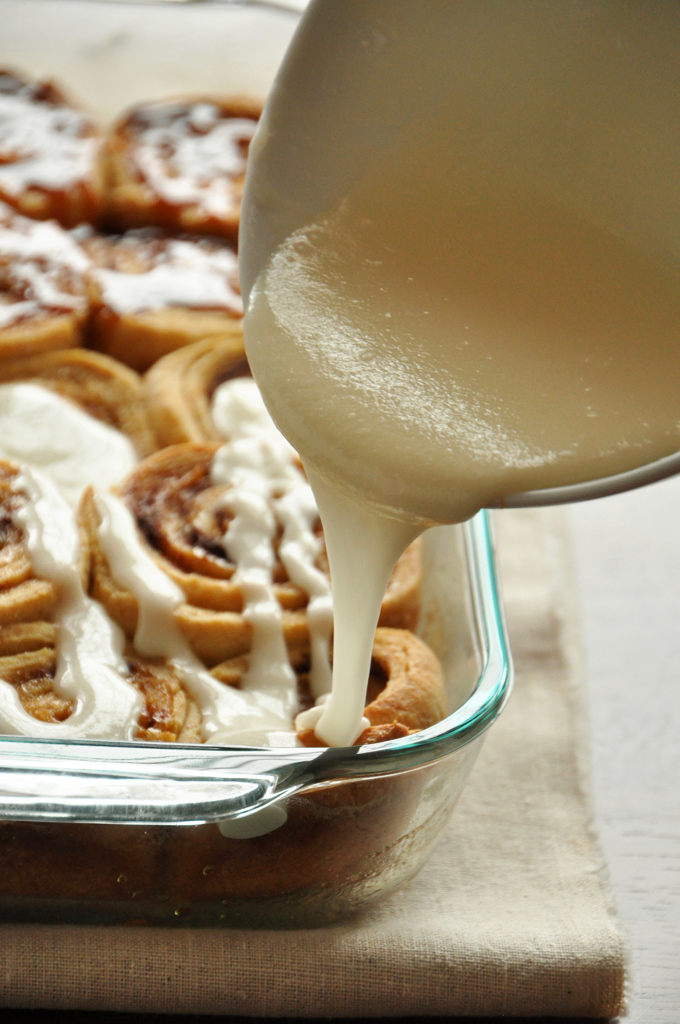 Vanlila Glaze Drizzling frosting onto a batch of Overnight Honey Wheat Cinnamon Rolls for a Christmas morning treat