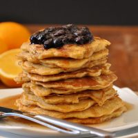 Plate stacked high with Whole Wheat Griddle Cakes topped with Blueberry Orange Compote and maple syrup
