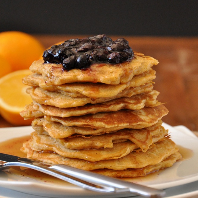 Plate stacked high with Whole Wheat Griddle Cakes topped with Blueberry Orange Compote and maple syrup