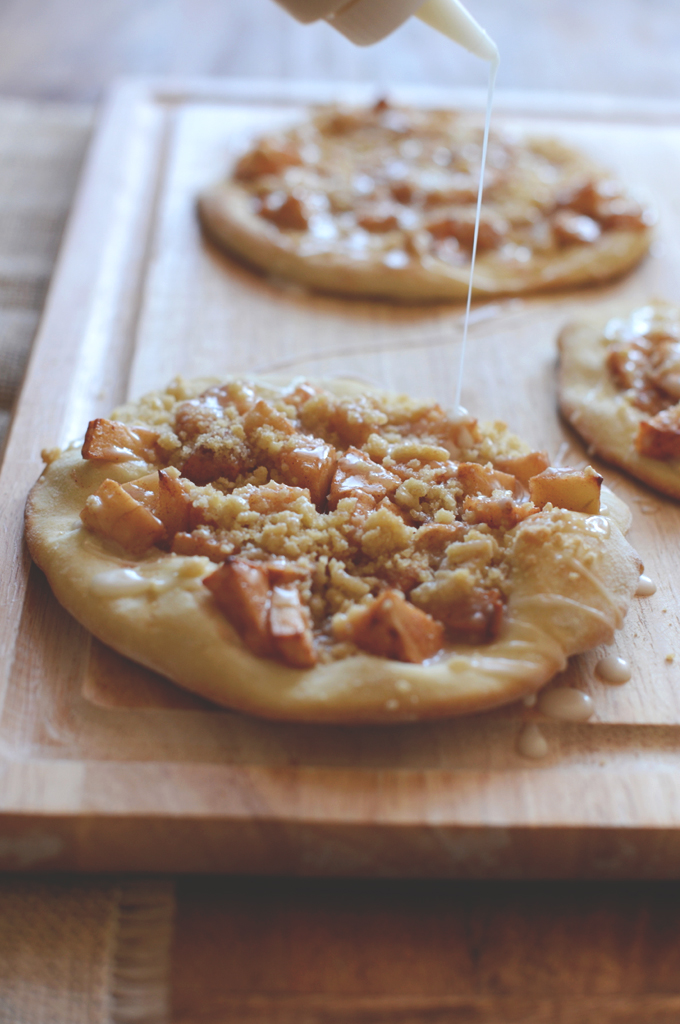 Drizzling Vanilla Frosting onto a cutting board filled with Apple Breakfast Pizzas