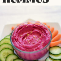 Bowl of vegan gluten-free roasted beet hummus with baby carrots and sliced cucumbers around it