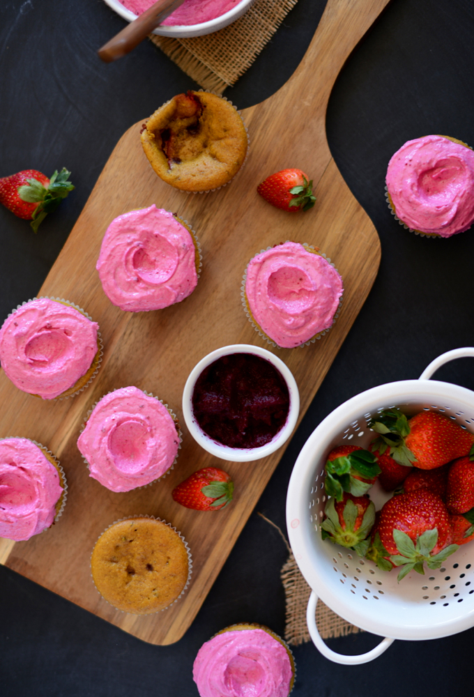 Cutting board with Vegan Strawberry Beet Cupcakes and a colander of fresh strawberries