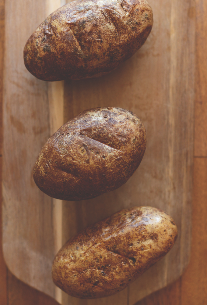 Three russet potatoes on a cutting board for making our Twice Baked Potatoes recipe