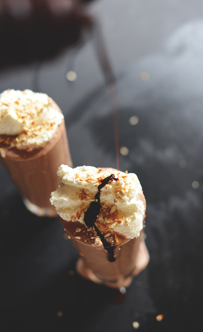 Drizzling hot fudge onto glasses of Vegan Pretzel Frozen Hot Chocolate