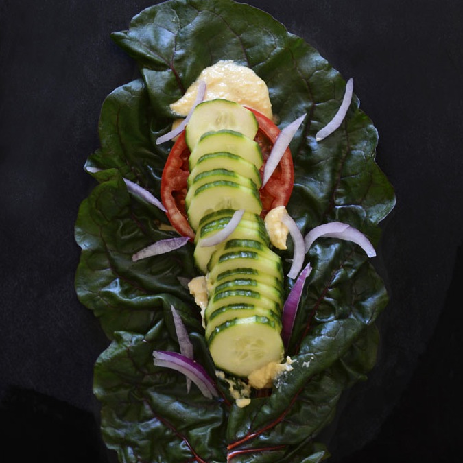 Vegan wrap made with a chard leaf, hummus, and fresh vegetables