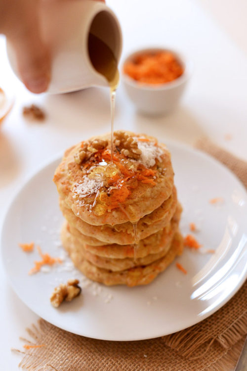 Pouring syrup over a stack of Carrot Coconut Pancakes for a vegan breakfast