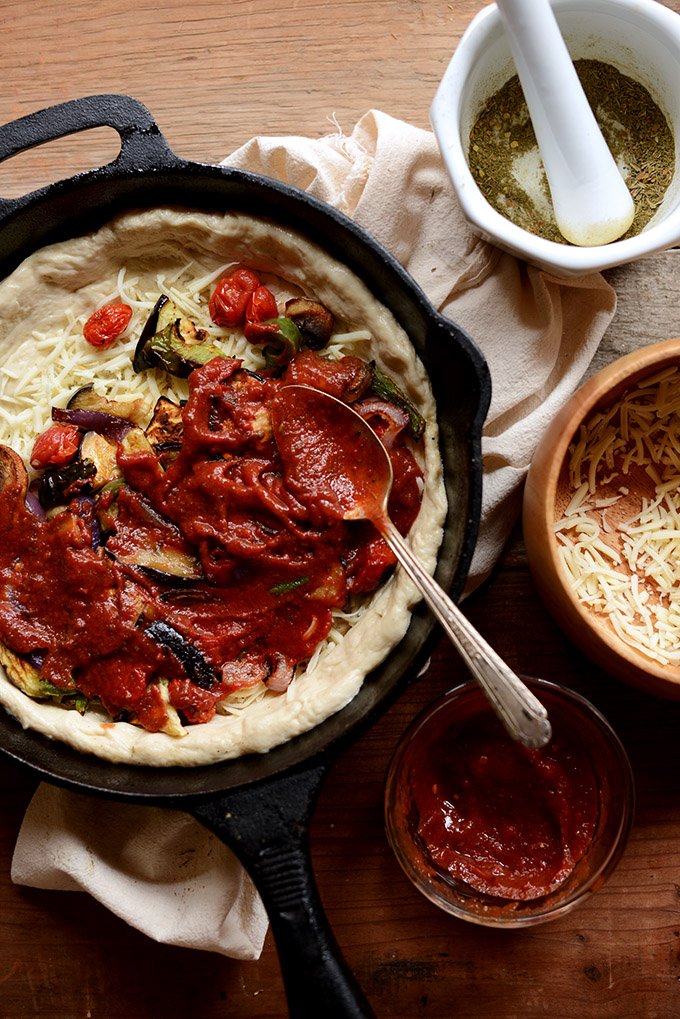 Spreading pizza sauce on top of roasted vegetables and shredded cheese