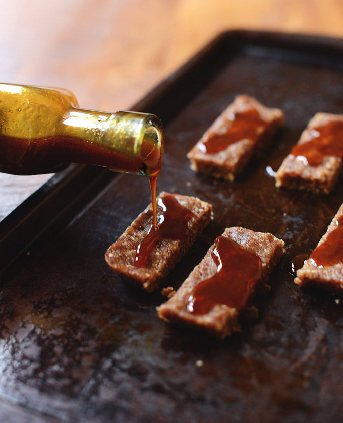 Pouring Vegan Caramel Sauce onto nougats for homemade snickers bars