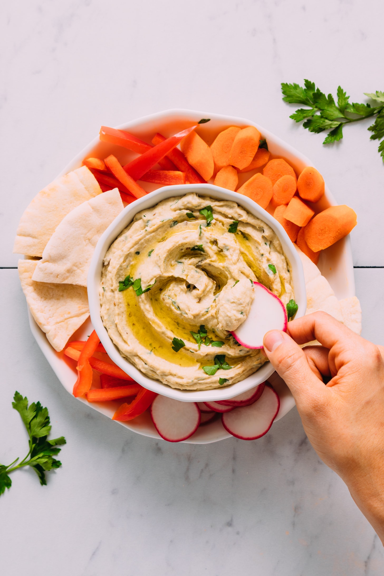 Dipping a radish slice into a bowl of eggplant dip
