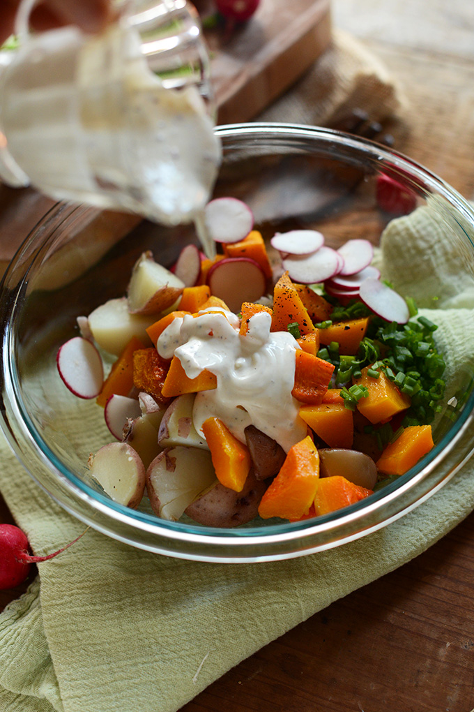 Pouring dressing onto a bowl of Butternut Squash Potato Salad