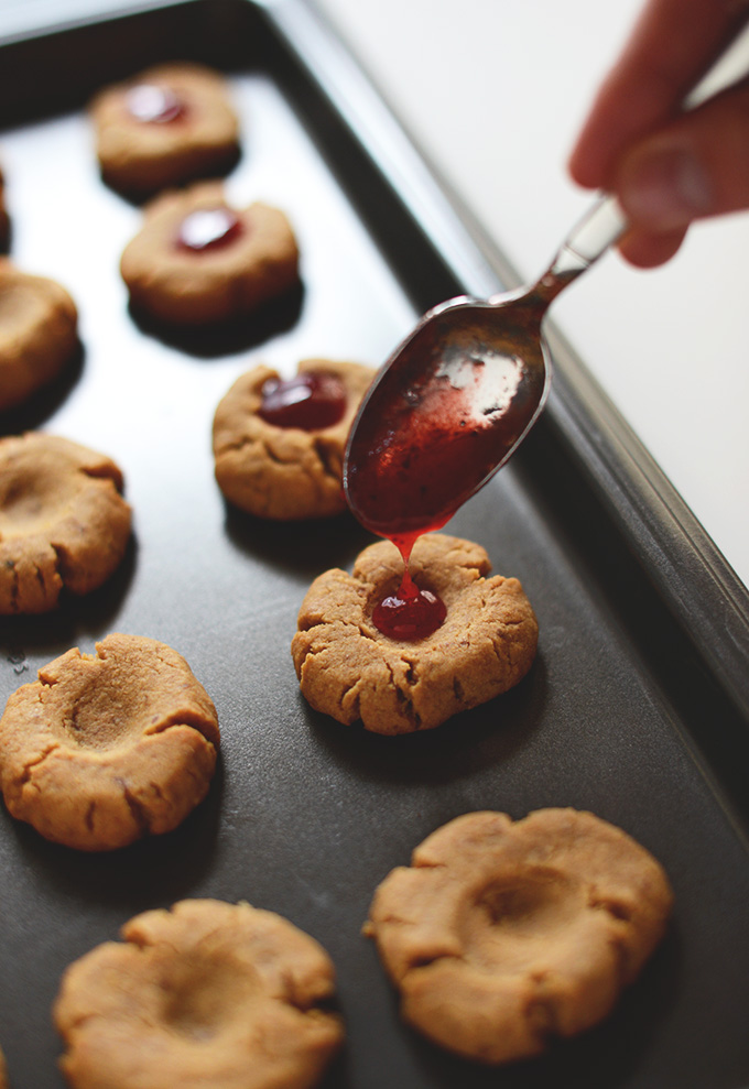 Drizzling jam into the center of Vegan PB&J Thumbprint Cookies