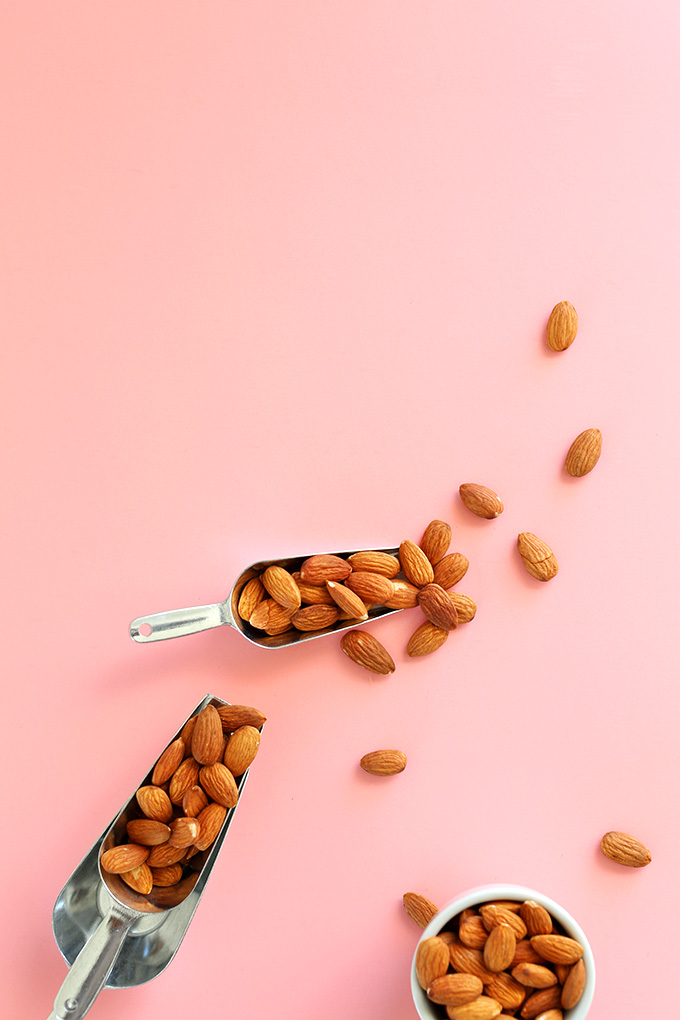 Bowl and scoops of almonds on a baking sheet for making homemade almond milk