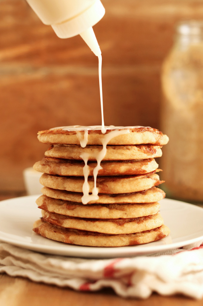 Drizzling icing onto a stack of Fluffy Vegan Yeasted Cinnamon Roll Pancakes