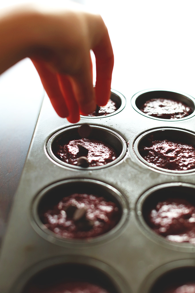 Sprinkling chocolate chips onto muffin tins filled with Vegan Chocolate Chocolate Chip Muffins
