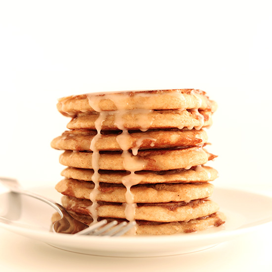 Plate with a tall stack of Vegan Cinnamon Roll Pancakes dripping with icing