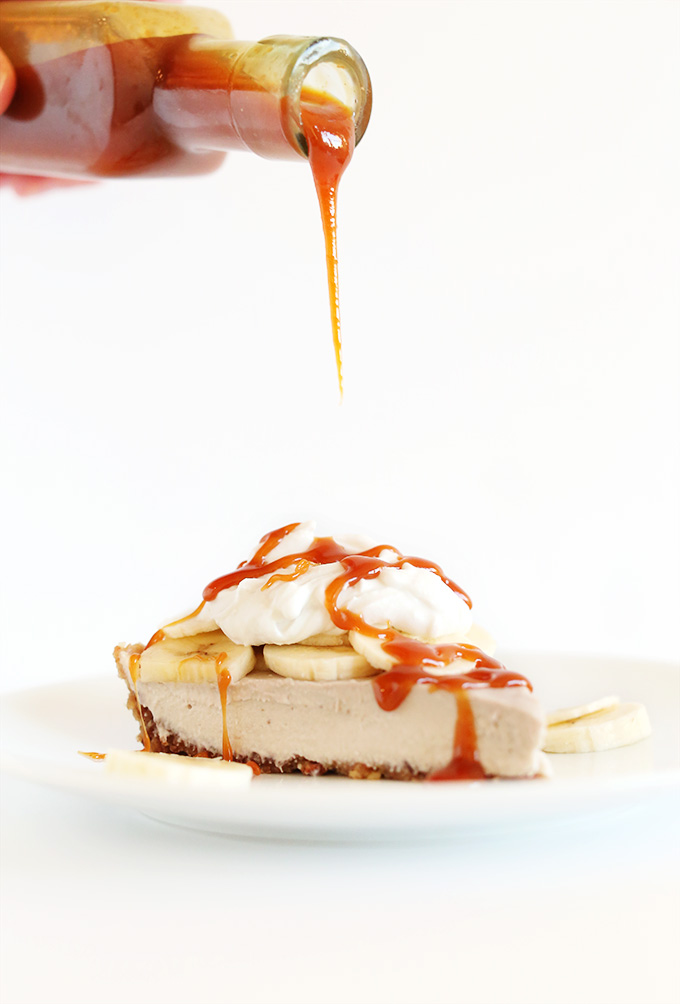 Drizzling vegan caramel sauce onto a slice of Raw Vegan Banana Cream Pie topped with coconut cream