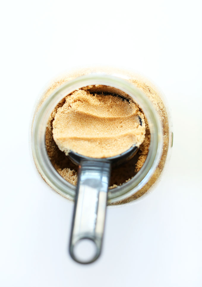 Measuring cup of brown sugar in a glass jar for adding to gluten free banana bread