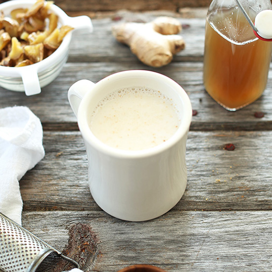 Mug of our Ginger Latte recipe beside fresh ginger and homemade ginger syrup