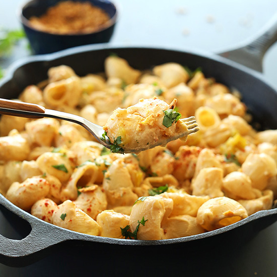 Using a fork to lift a bite of Vegan Green Chili Mac n Cheese from a skillet