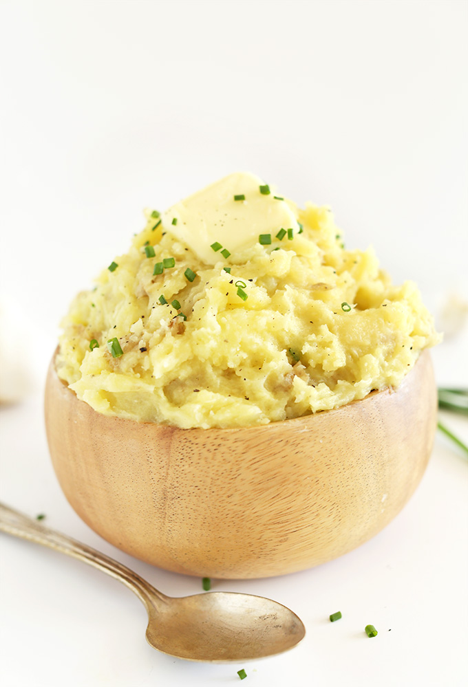 Wood bowl piled high with Vegan Mashed Potatoes topped with chives and black pepper