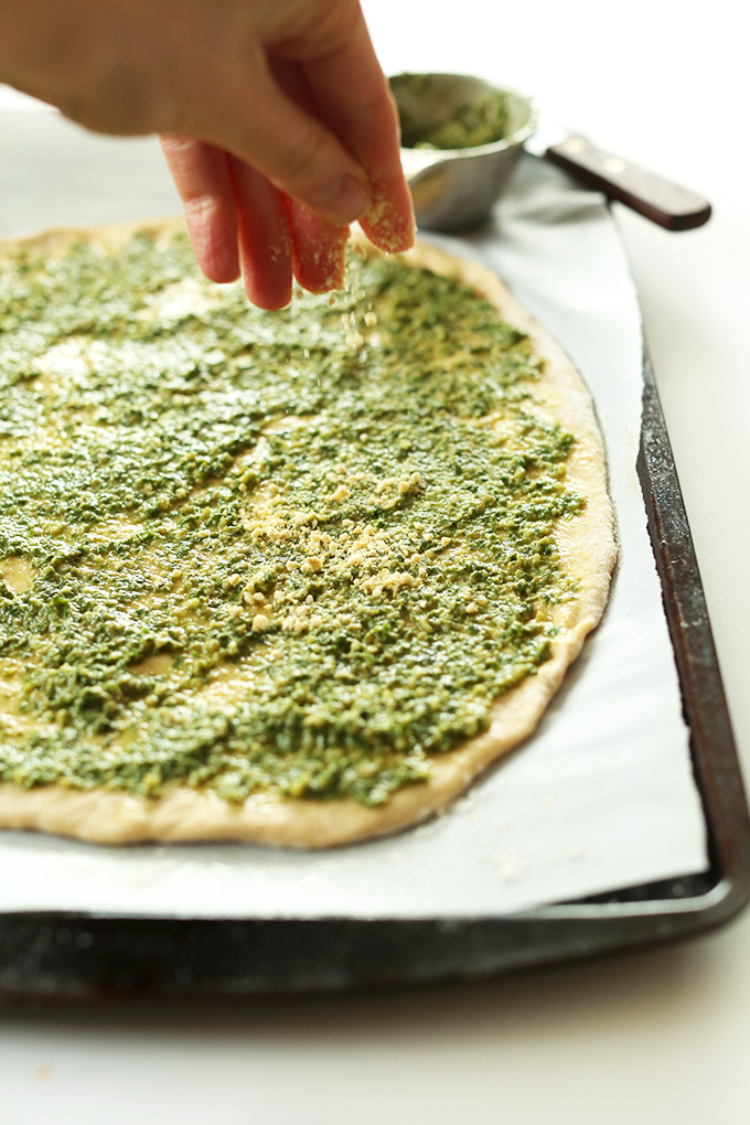 Sprinkling vegan parmesan cheese onto Vegan Pesto Breadstick dough