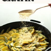 Sprinkling cashew parmesan over sliced zucchini for our easy and quick vegan zucchini gratin