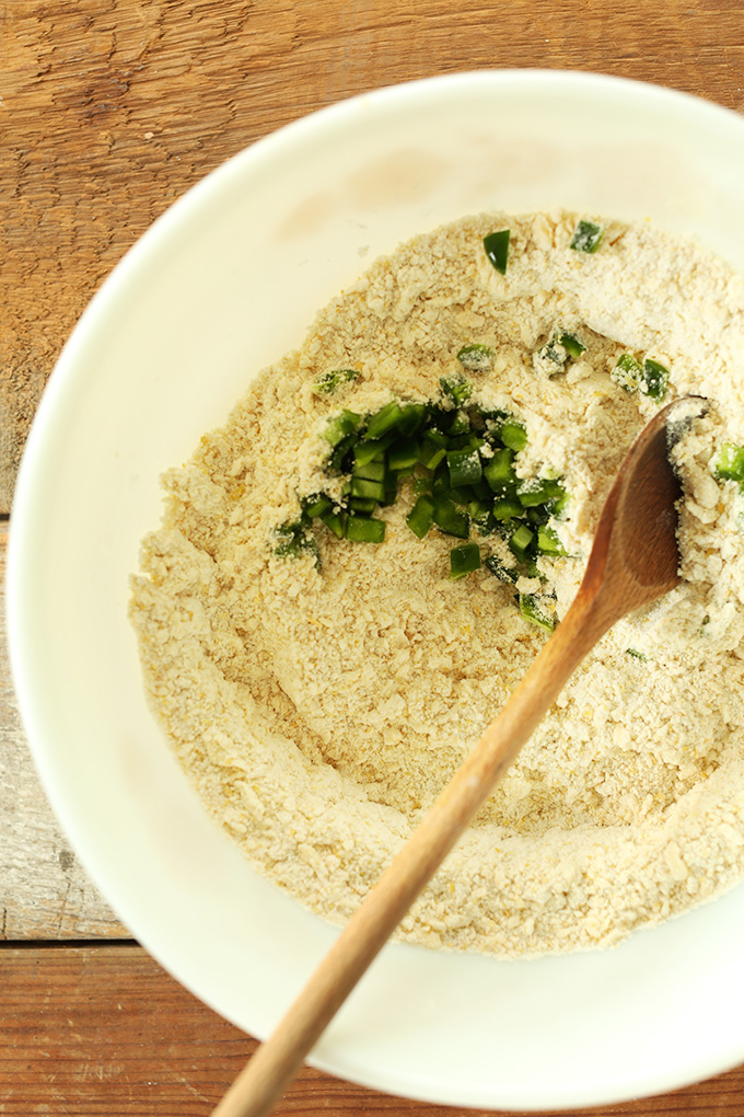Using a wooden spoon to stir diced jalapeno into dry ingredients