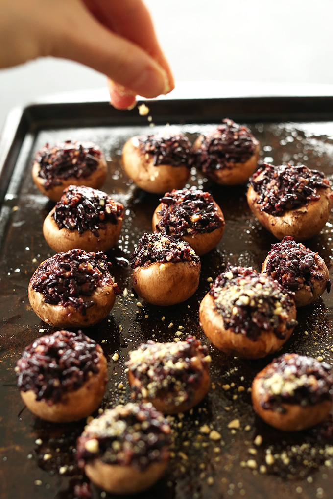 Sprinkling vegan parmesan onto stuffed mushrooms