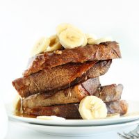 Slices of Vegan Banana French Toast piled high and topped with sliced bananas and syrup
