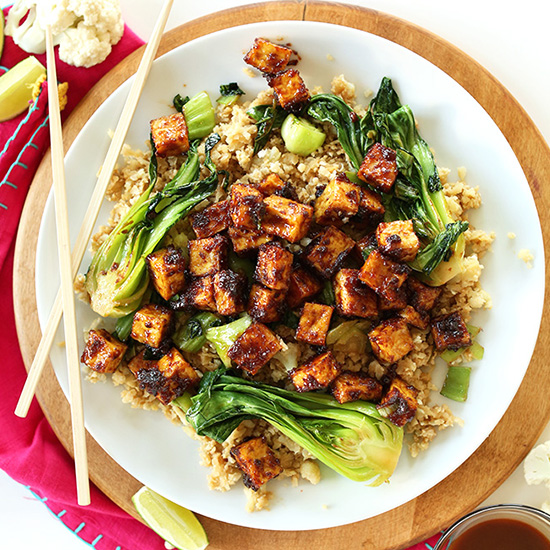 Chopsticks resting on a plate of Crispy Peanut Tofu over Cauliflower Rice Stir-Fry