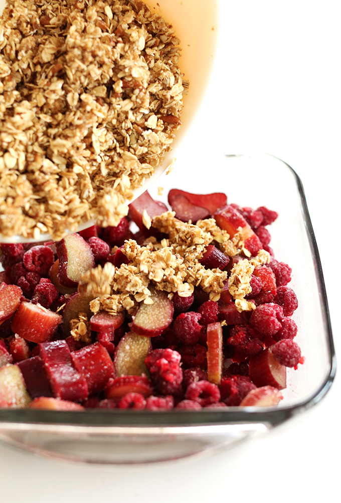 Pouring oat topping onto vegan Raspberry Rhubarb Crisp