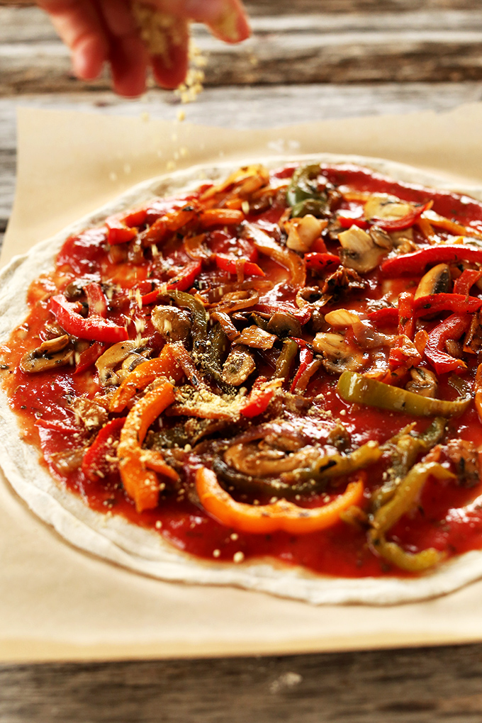 Sprinkling nutritional yeast onto pizza for homemade vegan pizza night