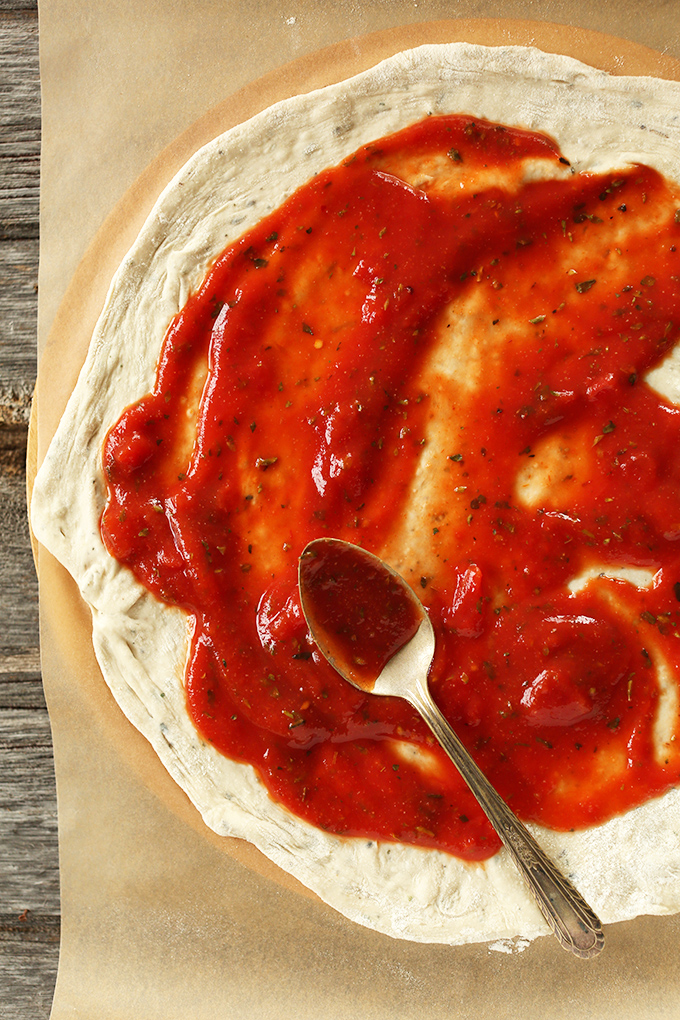 Using a spoon to spread pizza sauce onto dough for the Best Vegan Pizza