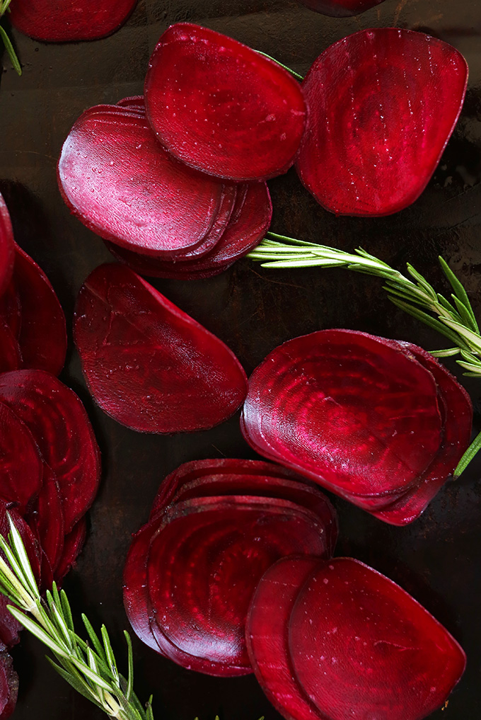 Thinly sliced vibrant red beets with rosemary on a baking sheet
