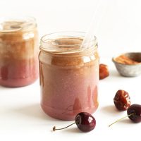 Two jars of Chocolate Cherry Almond Milk beside dates, cocoa powder, and fresh cherries
