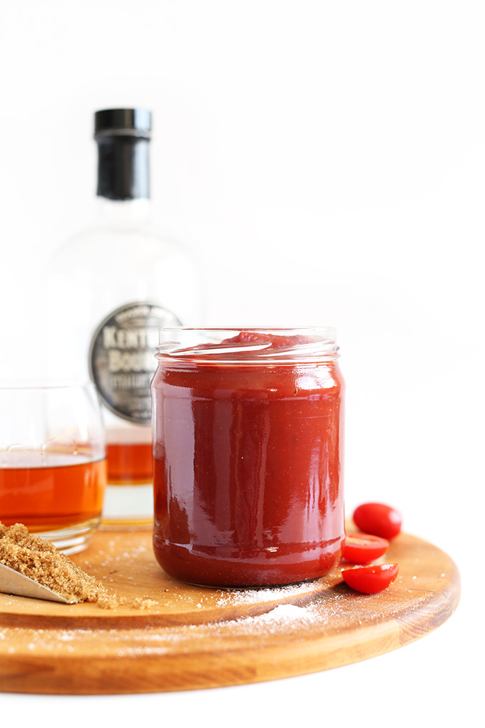 Side shot of a jar of whiskey BBQ ketchup and ingredients used to make it