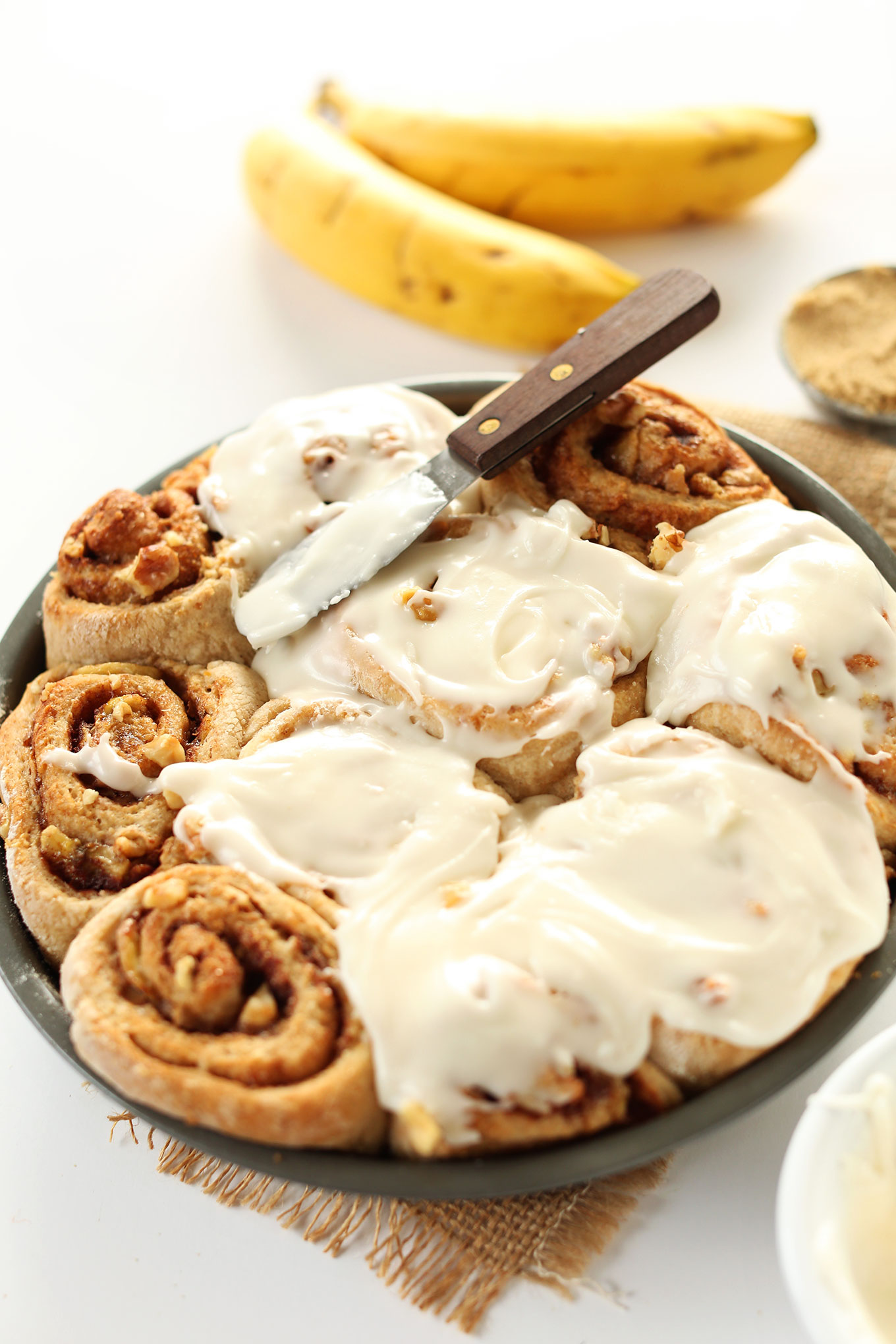 Spreading icing over a batch of freshly baked Vegan Banana Bread Cinnamon Rolls