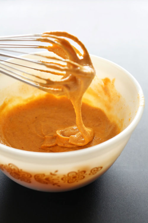 Vegan Mexican Queso falling off a whisk into a bowl