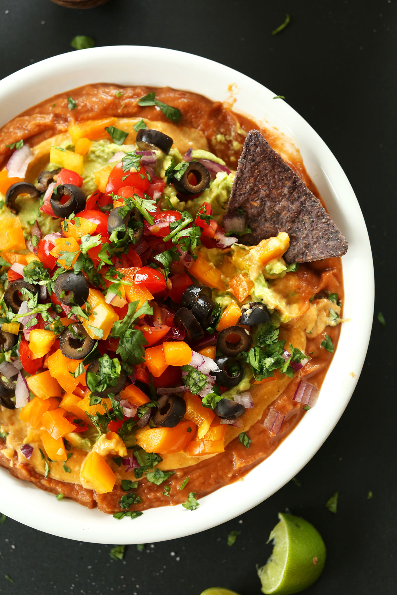 Blue corn tortilla chip dipped into a big bowl of Vegan 7-Layer Mexican Dip
