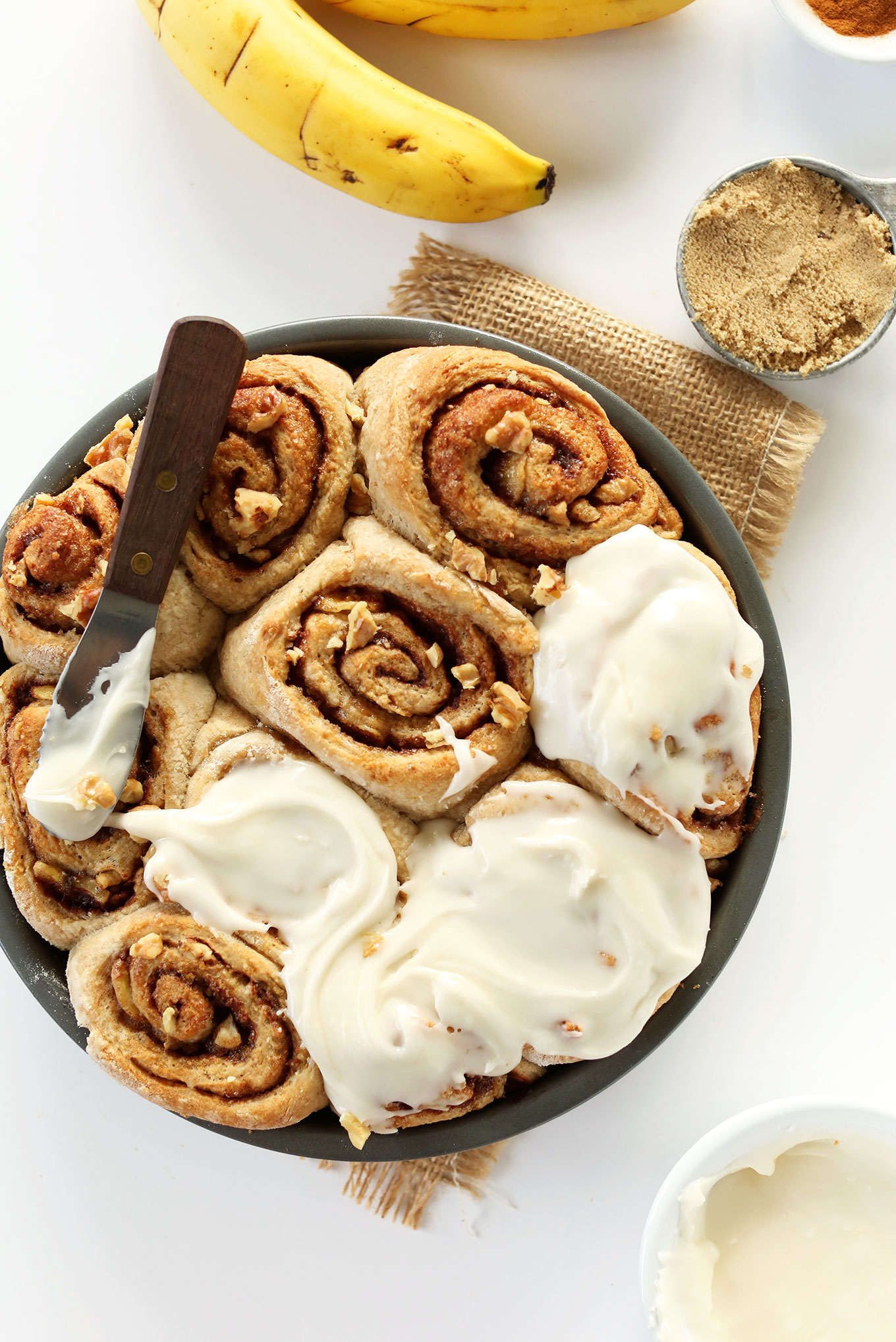 Spreading icing over freshly baked Vegan Banana Bread Cinnamon Rolls