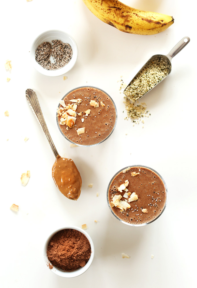 Two homemade recovery drinks surrounded by hemp seeds, chia seeds, banana and a spoonful peanut butter